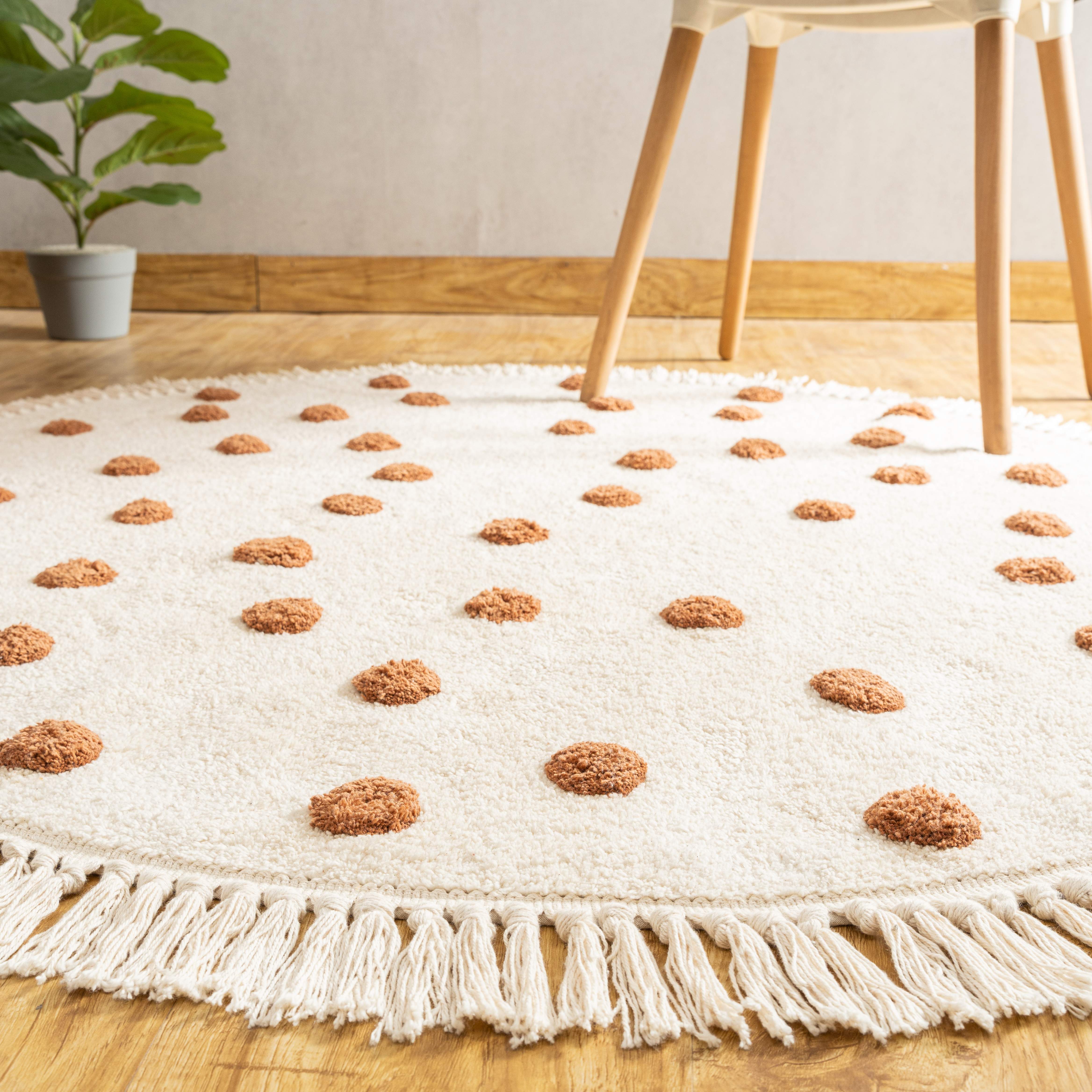 Handmade cotton polka dot rug with charming fringes, showcasing its size with a book and potted plant for scale.